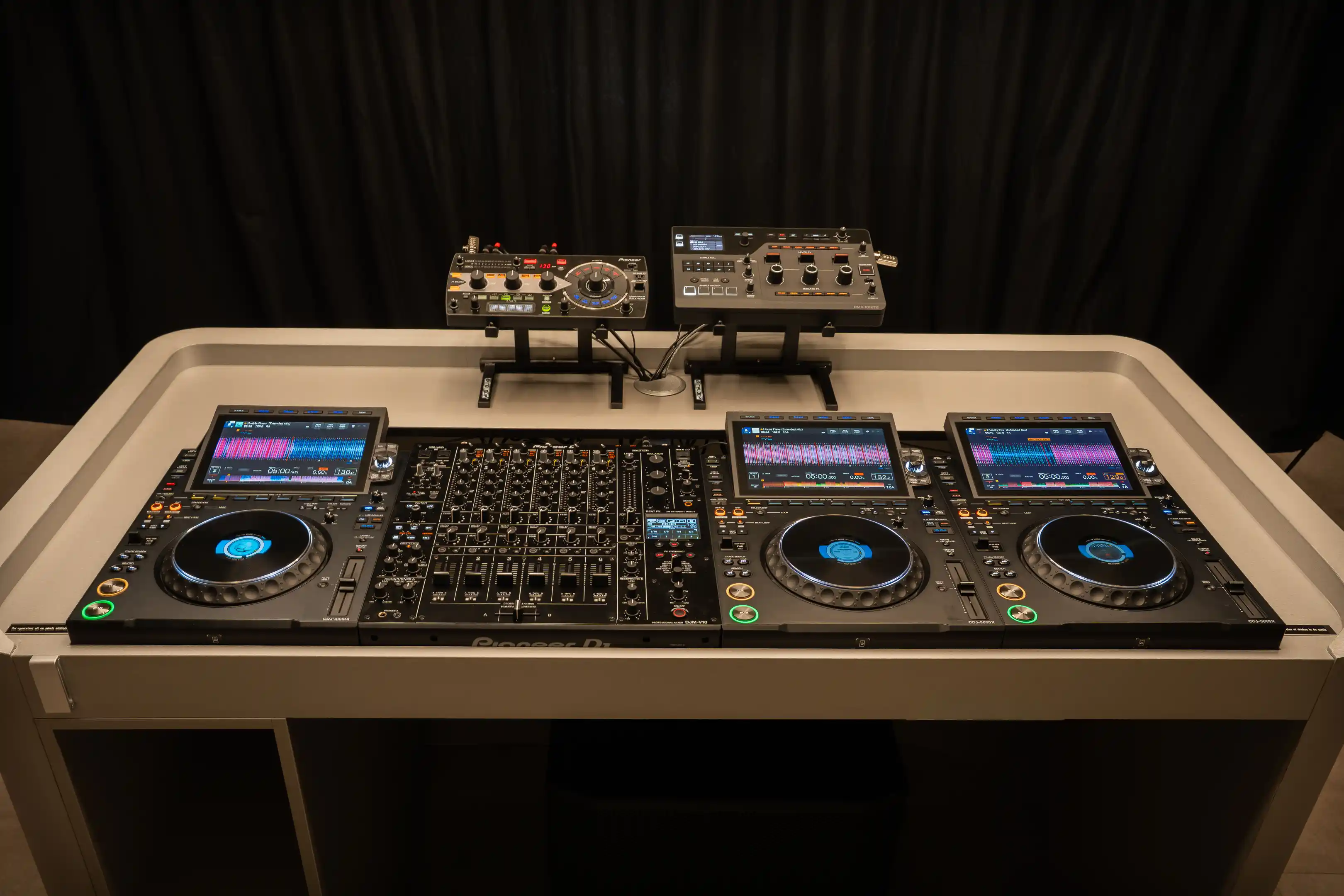 De DJ-booth van voren: drie CDJ-3000X-spelers, de DJM-V10 en twee effect units op een standaard