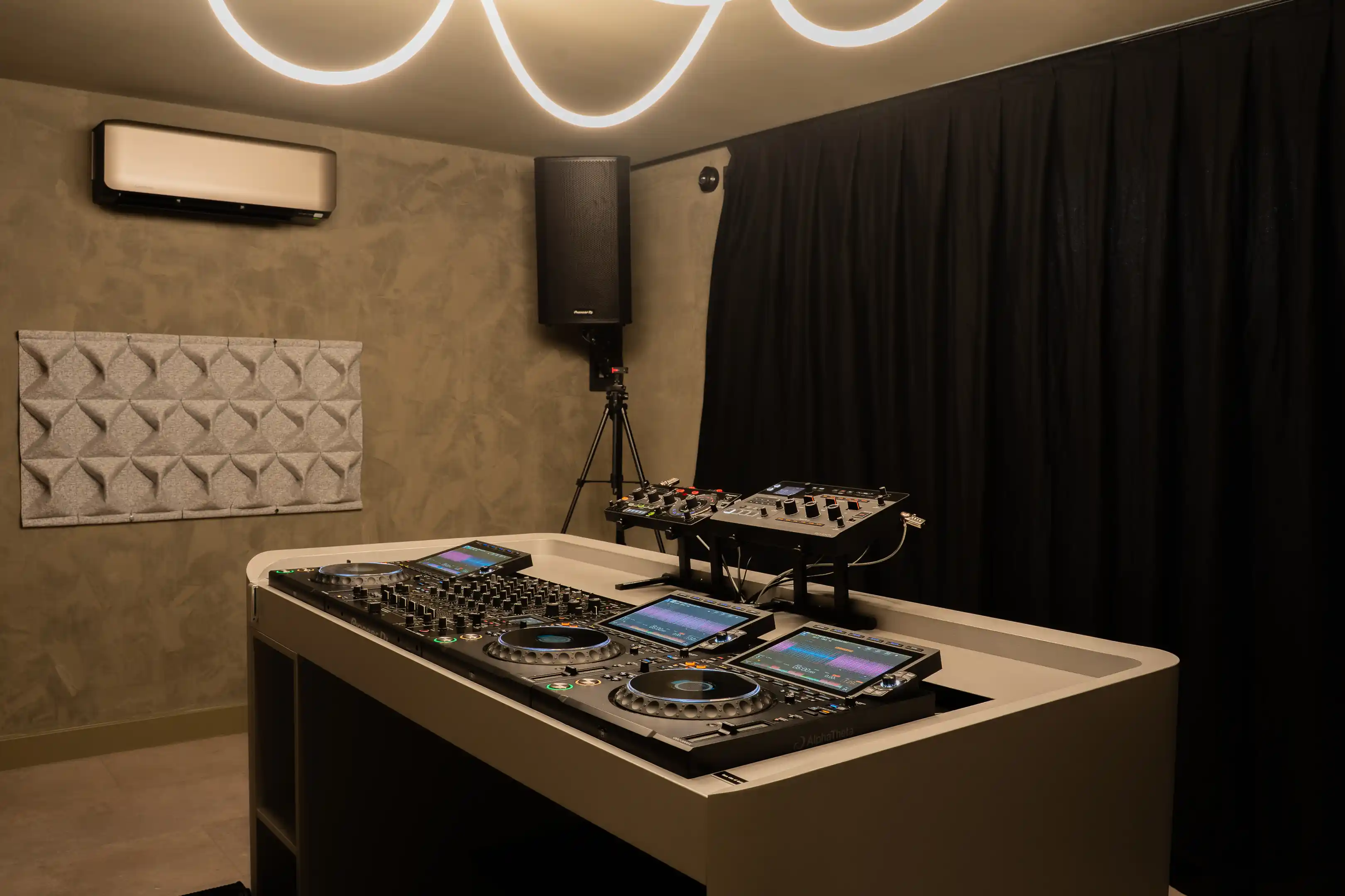 De DJ-booth met neonlicht erboven, een speaker op een statief en zwarte gordijnen